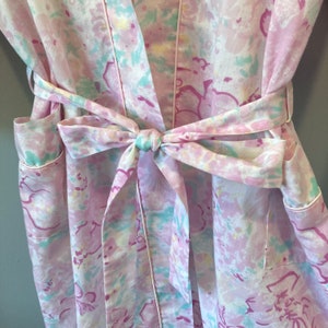 May include: A pink and white floral robe with a matching tie belt. The robe has a light blue trim and a light blue and pink floral pattern.