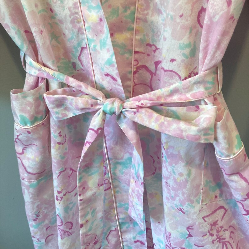 May include: A pink and white floral robe with a matching tie belt. The robe has a light blue trim and a light blue and pink floral pattern.