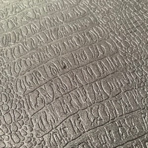 Puede incluir: Primer plano de una superficie gris texturizada con un patr&oacute;n repetitivo de letras en relieve. La superficie tiene un sutil patr&oacute;n de piel de cocodrilo.