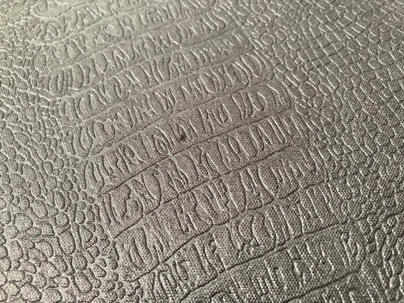 Puede incluir: Primer plano de una superficie gris texturizada con un patr&oacute;n repetitivo de letras en relieve. La superficie tiene un sutil patr&oacute;n de piel de cocodrilo.