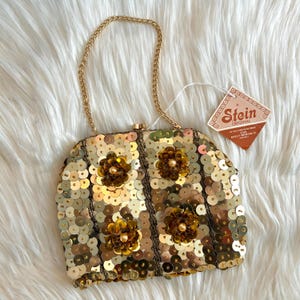May include: A vintage gold sequin handbag with a gold chain handle. The bag features vertical stripes and is adorned with four flower embellishments. A Stein Original tag is attached.