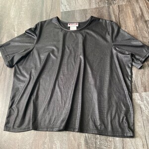Puede incluir: Camiseta negra de manga corta con un acabado texturizado de imitaci&oacute;n de cuero. La camiseta tiene un cuello redondo y un corte holgado.