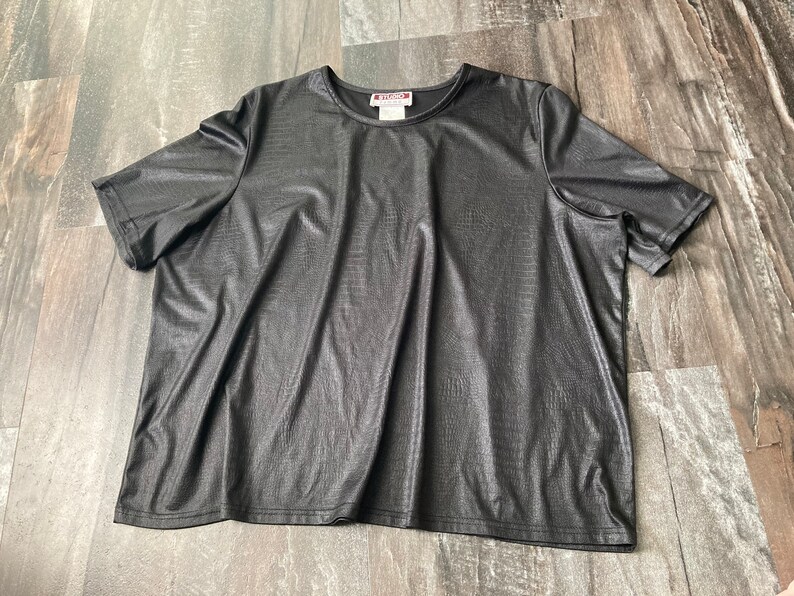 Puede incluir: Camiseta negra de manga corta con un acabado texturizado de imitaci&oacute;n de cuero. La camiseta tiene un cuello redondo y un corte holgado.