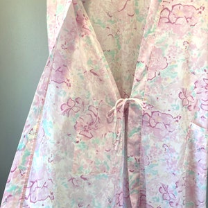 May include: A white robe with a pink and green floral pattern. The robe has a tie at the waist and a pocket on the right side.