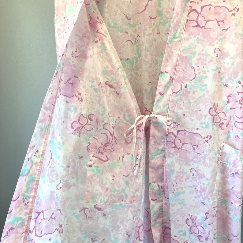 May include: A white robe with a pink and green floral pattern. The robe has a tie at the waist and a pocket on the right side.
