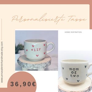 Könnte beinhalten: Weißer Keramikbecher mit Henkel, verziert mit kleinen roten Herzen und dem Namen "elly" in Rot. Der Becher steht auf einem kleinen Holzständer. Das Bild zeigt auch eine zweite Tasse mit dem Text "mom of two".