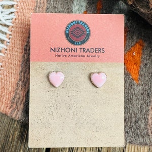May include: A pair of pink heart-shaped earrings on a card that reads "Nizhoni Traders Native American Jewelry".
