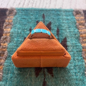 May include: A turquoise and silver ring in a triangular orange velvet ring box.