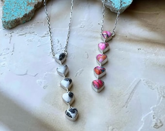 May include: Two silver necklaces with heart-shaped pendants. One necklace features black and white patterned hearts, while the other showcases pink and red hearts. The pendants are strung on delicate silver chains, creating a romantic and elegant look.