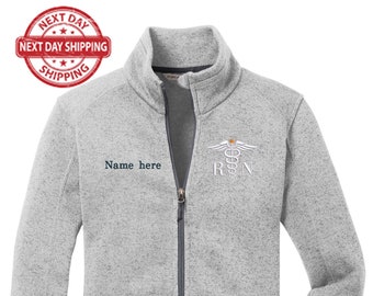 May include: A gray fleece zip-up jacket with a white embroidered caduceus and the letters "RN" on the right side of the chest. The text "Name here" is embroidered on the left side of the chest.