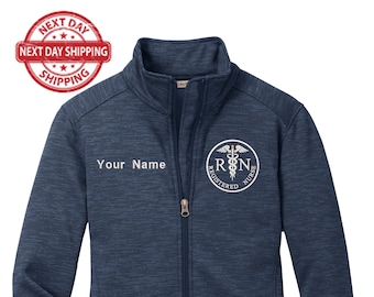 May include: A navy blue fleece jacket with a zipper closure and two zippered pockets. The jacket has a white embroidered design on the left chest that says "Registered Nurse" and includes a caduceus symbol. The text "Your Name" is embroidered on the left chest.