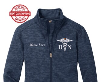 May include: A navy blue zip-up jacket with a white embroidered medical symbol and the letters "RN" on the right side of the chest. The text "Name here" is embroidered on the left side of the chest.