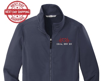 May include: Navy blue zip-up jacket with a stand-up collar. Features a red heart-shaped EKG design and the name "Olivia, BSN RN" embroidered on the chest. Includes two zippered pockets and a full-length zipper.