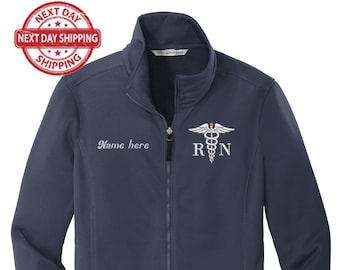May include: A navy blue soft-shell jacket with a zipper closure. The jacket has a white embroidered medical symbol and the letters "RN" on the right side of the chest. The text "Name here" is embroidered on the left side of the chest.