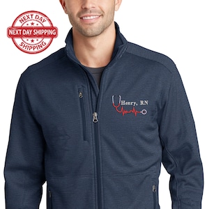 May include: A navy blue fleece jacket with a zipper closure and two zippered pockets. The jacket has a red embroidered stethoscope with a heartbeat and the text "Henry, RN".
