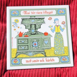 May include: Square ceramic tile with a vintage illustration of a green stove, a woman, and text in Swedish. The stove has heart-shaped details and a red teapot. The woman wears a yellow vest and a long skirt.
