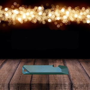 May include: A teal blue metal multi-tool with a bottle opener, a flathead screwdriver, and a Phillips head screwdriver. The multi-tool is sitting on a wooden surface with a blurred background of golden lights.
