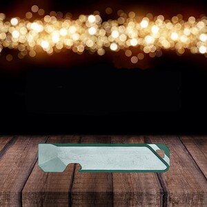 May include: A silver and green multi-tool with a bottle opener, a flathead screwdriver, and a pry bar. The tool is sitting on a wooden surface.