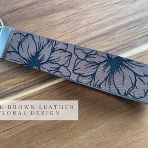 May include: Dark brown leather key chain with a floral design.  The key chain has a silver key ring.