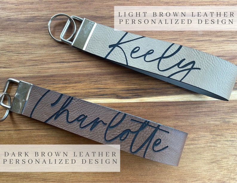 May include: Two leather keychains with personalized names. The top keychain is light brown leather with the name "Keely" written in black cursive. The bottom keychain is dark brown leather with the name "Charlotte" written in black cursive.
