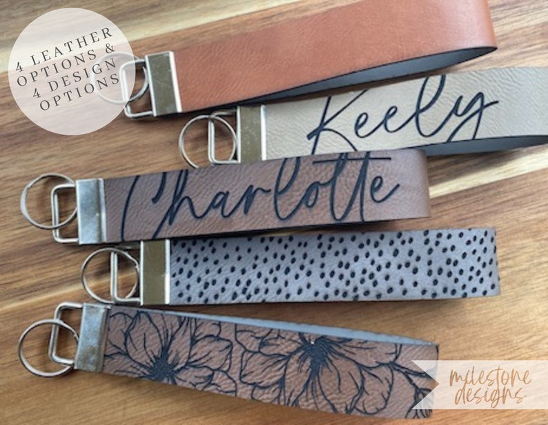 May include: Four leather keychains with different designs. The keychains are brown, beige, gray, and brown with a floral pattern. The keychains have metal rings and are personalized with the names "Keely", "Charlotte", and "milestone designs".