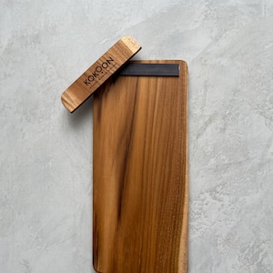 May include: A rectangular wooden cutting board with a magnetic knife holder. The knife holder is made of wood and has the word "KOKOON" printed on it. The cutting board is made of a light brown wood.
