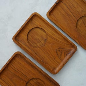 May include: Three rectangular wooden trays with a circular indentation in the centre. The trays are made of light brown wood with a natural grain pattern.