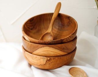 May include: A set of four wooden bowls stacked on top of each other. The bowls are made of natural wood and have a light brown colour. A wooden spoon is resting on top of the bowls.