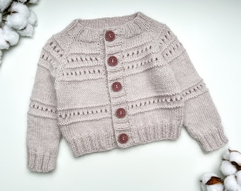 May include: A pale pink knitted cardigan with a button-up front and a delicate lace pattern. The cardigan has five brown buttons.