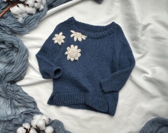 May include: A blue knitted sweater with white crocheted flower embellishments.
