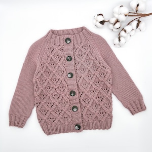 May include: A dusty rose knitted cardigan with a button-up front and a delicate openwork pattern.