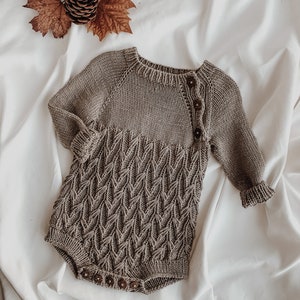 May include: A brown knitted baby onesie with a leaf pattern and wooden buttons.