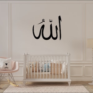 Könnte beinhalten: Ein weißes Babybett mit einem schwarz-weißen gemusterten Teppich davor. Die Wand hinter dem Babybett hat ein schwarzes arabisches Kalligraphie-Design, das "Allah" sagt.