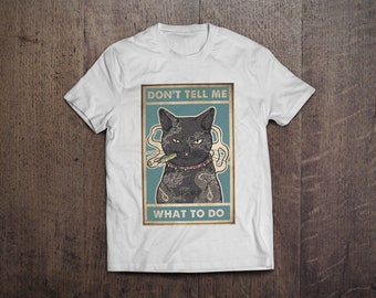 May include: White t-shirt featuring a graphic of a black cat with tattoos, smoking a cigarette. The cat is wearing a pink collar. The text "DON'T TELL ME WHAT TO DO" is above the cat.