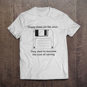 Könnte beinhalten: Weißes T-Shirt mit einer schwarzen Grafik einer Diskette und dem Text: "Disketten sind wie Jesus. Sie starben, um die Ikone des Speicherns zu werden."