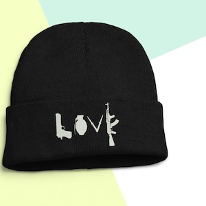 May include: Black beanie with a white graphic of the word "LOVE" spelled out using images of a gun, a grenade, a knife, and a rifle.