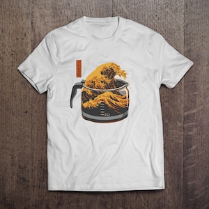 May include: White t-shirt featuring a coffee pot design with a wave graphic in shades of gold and brown. The design incorporates Japanese-style art elements. The shirt has a crew neck and short sleeves.