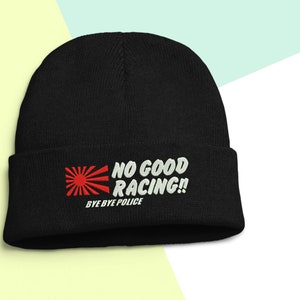 May include: Black beanie hat featuring the embroidered text "NO GOOD RACING!! BYE BYE POLICE" in white and red. The design includes a red sunburst graphic. The hat is made of a soft, knitted material.