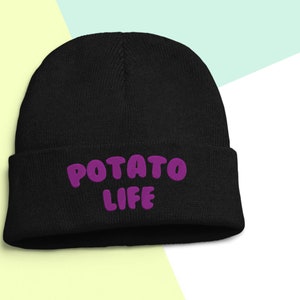 Könnte beinhalten: Schwarze Mütze mit dem Text "POTATO LIFE" in Lila.
