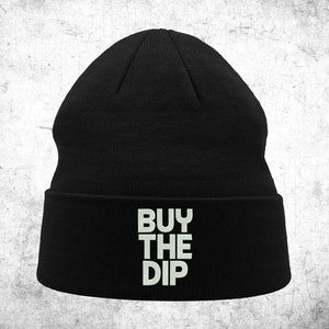Può includere: Berretto nero con un designo ricamato bianco che dice "BUY THE DIP".