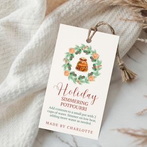 May include: A cream-colored tag with a watercolor illustration of a potpourri wreath. The tag reads "Holiday Simmering Potpourri" with instructions and "Made by Charlotte" at the bottom. A twine loop is at the top.