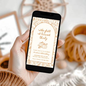 Puede incluir: Un teléfono inteligente muestra una invitación de cumpleaños con temática otoñal. El texto "The fall I turned thirty" se muestra dentro de un arco, con ilustraciones de calabazas y hojas. La invitación también incluye detalles del evento y una solicitud de confirmación.