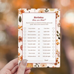 Peut inclure: Une carte de jeu d'anniversaire sur le thème de l'automne avec le texte "Birthday this or that ?" dans une police décorative. La carte présente une liste de choix comme "Cozy sweater or Cute dress" et est ornée de feuilles et de fleurs d'automne.