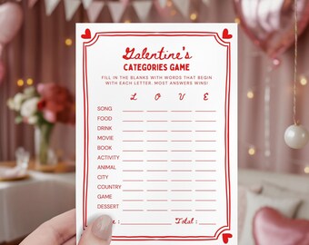 May include: A white Valentine's Categories Game card with red text and a decorative border. The card features prompts for song, food, drink, movie, book, activity, animal, city, country, game, and dessert. The card is held by a person.