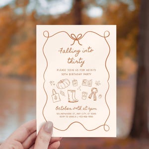 May include: A beige invitation with brown text and illustrations, held by a hand. The text reads "Falling into thirty" and invites guests to Heidi's 30th birthday party on October 24th at 6 pm. Includes address and RSVP information.