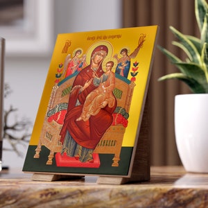 May include: A wooden icon with a gold background depicting the Virgin Mary and baby Jesus. The icon is framed in a dark wood and has a gold inscription at the top. The icon is on a wooden stand.
