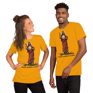 May include: Mustard yellow t-shirts featuring a graphic of a religious figure with a halo, holding a cross, and standing on a snake. The text "I TREAD WHERE I PLEASE" is below the image. The shirts are worn by two people.