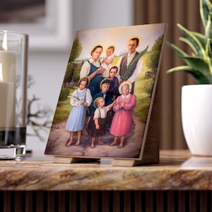 Puede incluir: Una pintura enmarcada de una familia con siete personas. La familia está de pie en un campo con hierba verde y árboles. El padre sostiene una rama con hojas. La madre sostiene un bebé. Los niños están todos sonriendo. La pintura está en un soporte de madera.