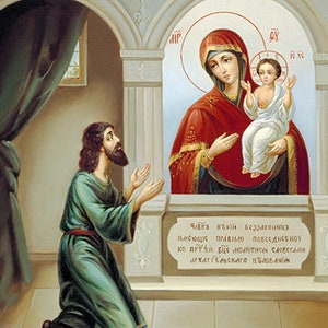 May include: A religious icon depicting the Virgin Mary holding a baby Jesus. The icon is painted in a traditional style with gold accents. A man in a green robe kneels in prayer before the icon. The text on the icon reads "ФБРАЗА ПРСЕ БЦЫ НЕЧААННИЙ РАДОСТЬ" which translates to "The image of the Virgin Mary is a source of joy".