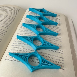 May include: Four blue plastic page holders with a geometric design. The page holders are designed to help keep your place in a book.